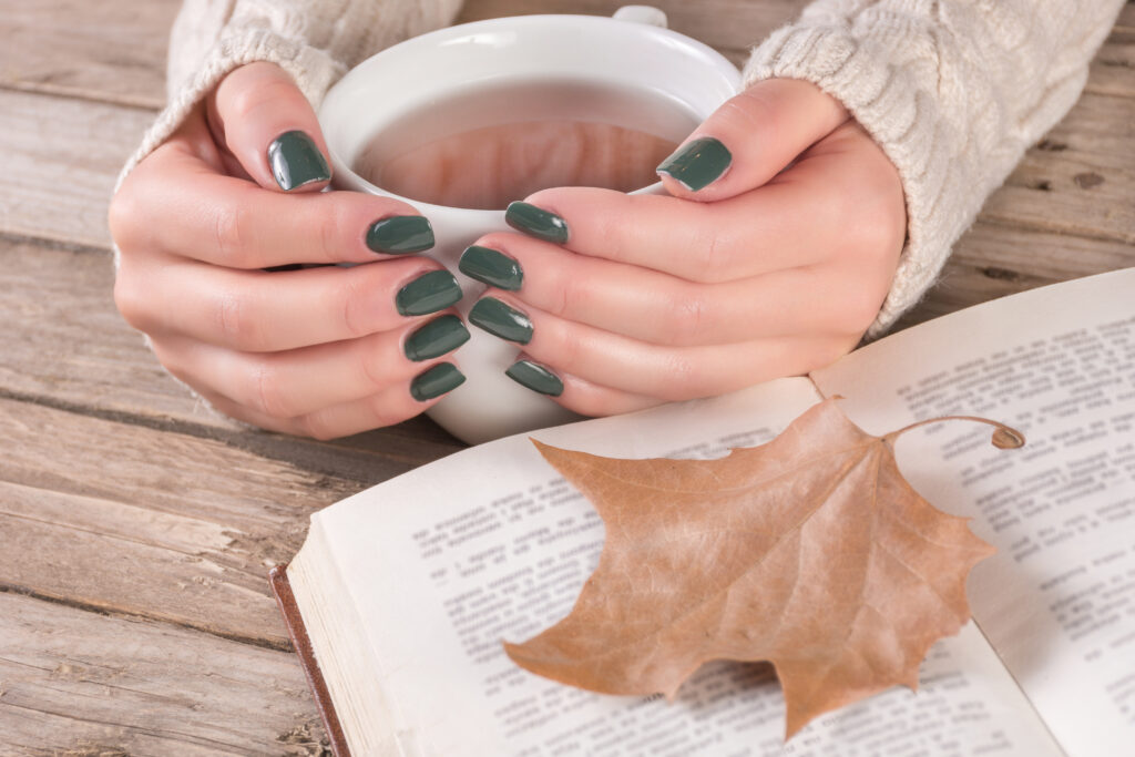 a lady holding a white mug and beautifully painted nails in fall nail polish colors