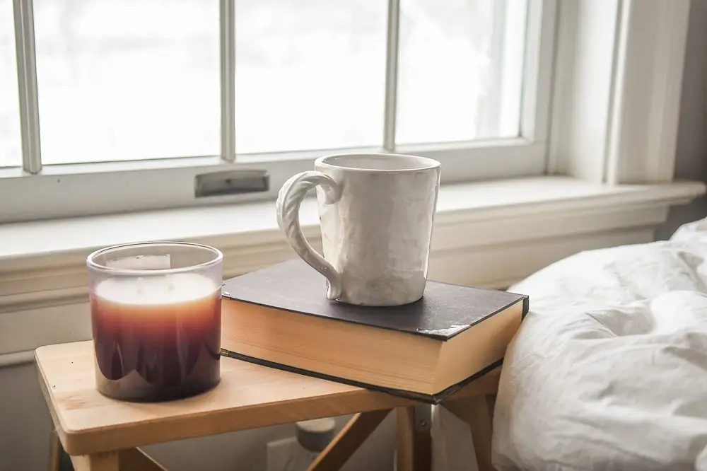 a white cup of coffee sitting on top of a black book next to a candle